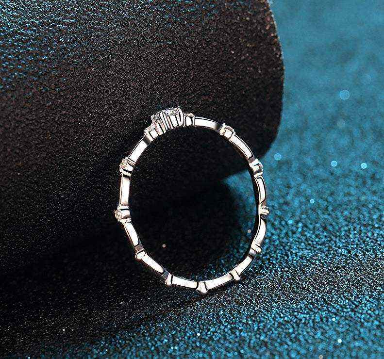 0.06 CTW DEW round moissanite decorative ring in platinum plated sterling silver with oval patterned band and prong-set side gems