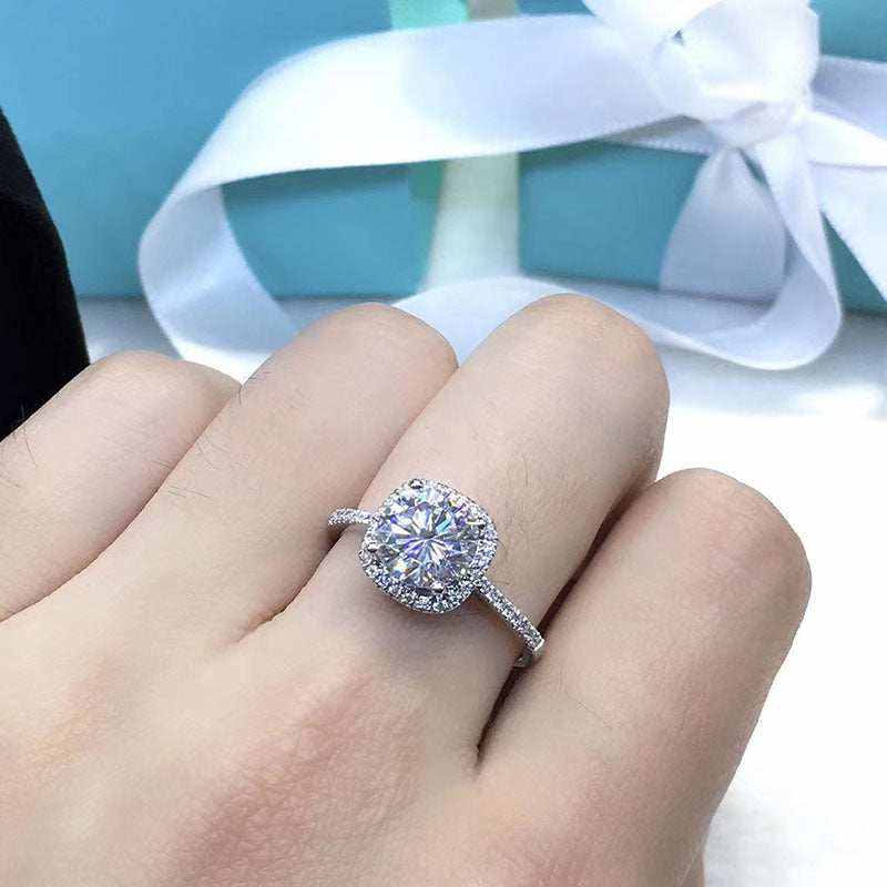 Close-up of a 1.5 CTW colorless round brilliant cut moissanite halo engagement ring in sterling silver with pavé accent stones, worn on a finger.