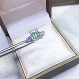1.8 CTW DEW emerald cut moissanite three stone engagement ring with tapered baguette accents in 18K gold plated sterling silver displayed in ring box