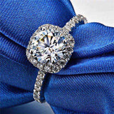 Close-up of a 1.5 CTW colorless round brilliant cut moissanite halo engagement ring in sterling silver with pavé accent stones on a blue fabric background