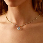 Close-up of a woman wearing a 14k gold chain necklace with a sky blue topaz pendant