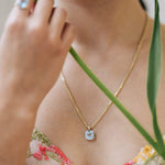 Close-up of a 14k gold necklace featuring a sky blue topaz pendant worn on a woman's neck