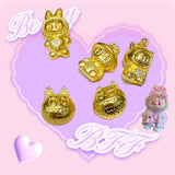 24K gold Labubu-inspired collectible doll-head pendants with sparkling moissanite gemstones on a pink and purple heart background