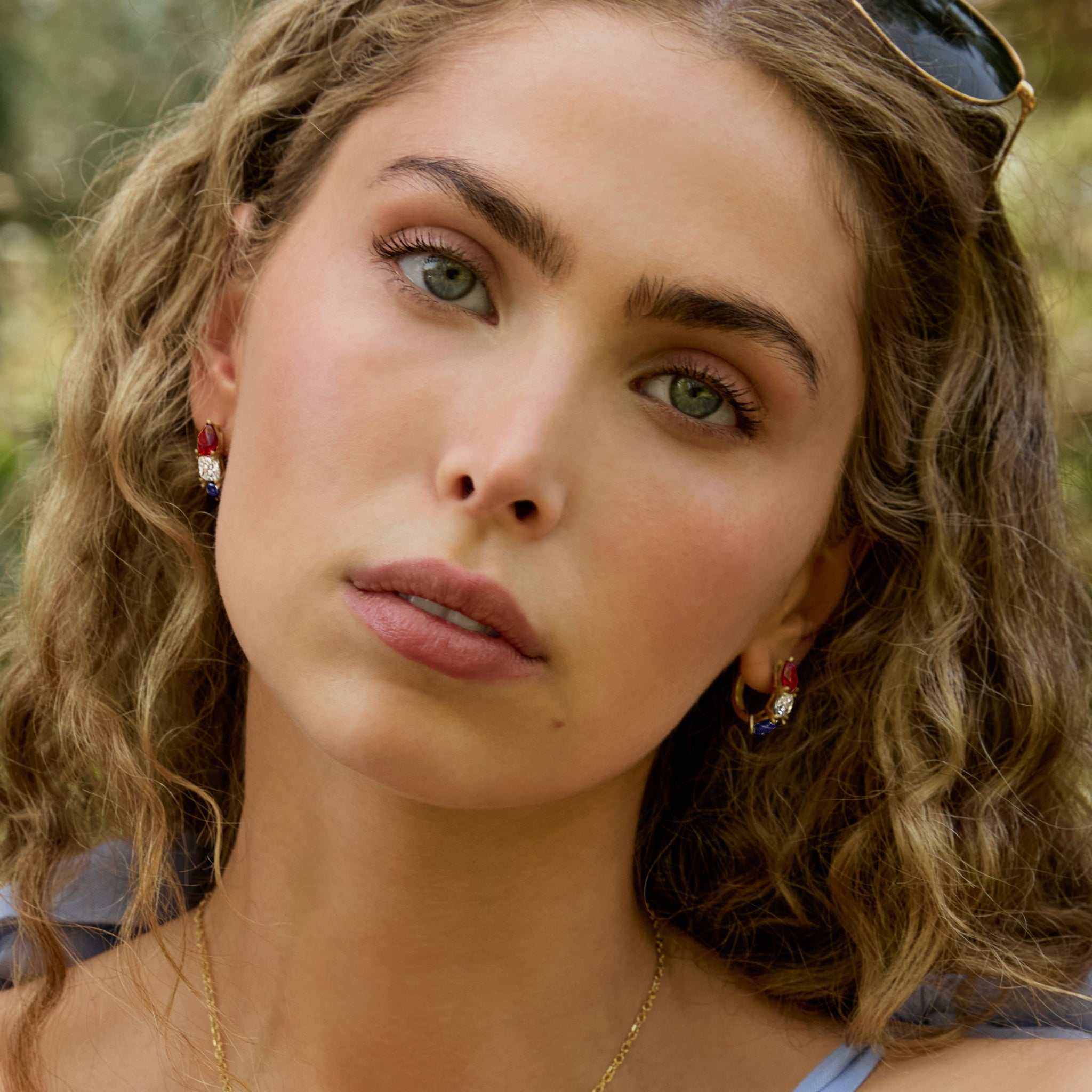 Close-up of a woman wearing Americana Signature Hoop Earrings with lab-grown ruby, diamond, and sapphire set in 14k gold.