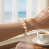 Pearl and gold bead stretch bracelet with white freshwater pearls on wrist by window and coffee cup