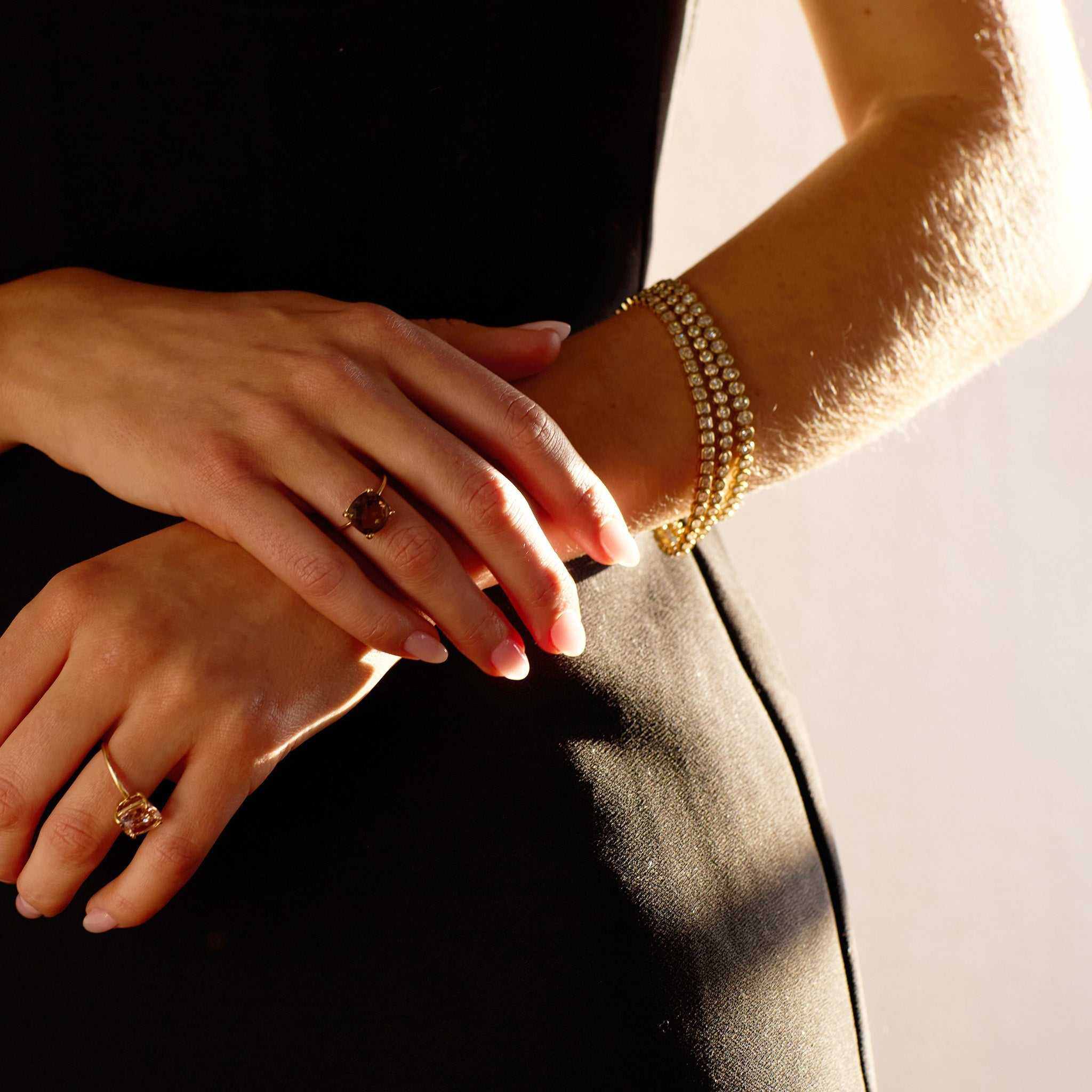 Close-up of a wrist wearing a 5 carat lab grown diamond tennis bracelet in yellow gold with rings, elegant and sparkling jewelry accessory