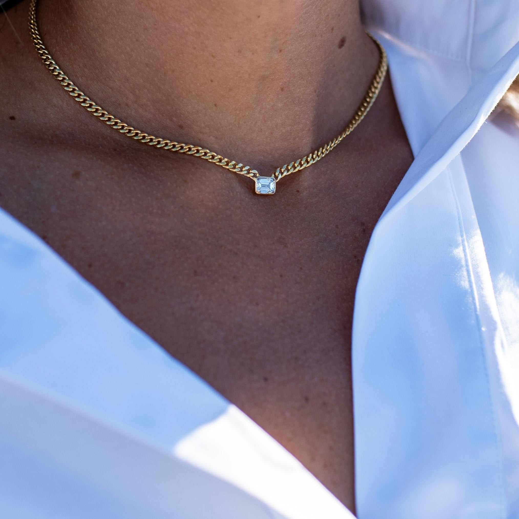 Emerald cut diamond bezel-set on 10k yellow gold Cuban chain necklace worn with white shirt