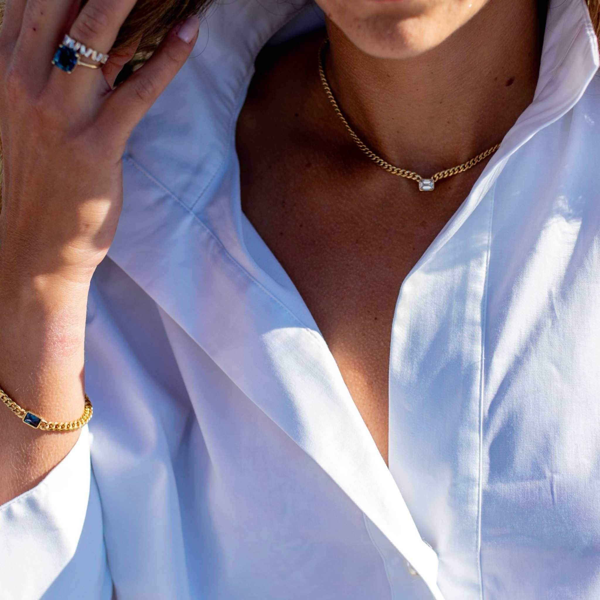 Emerald cut diamond bezel-set on a gold Cuban chain necklace worn with a white shirt.