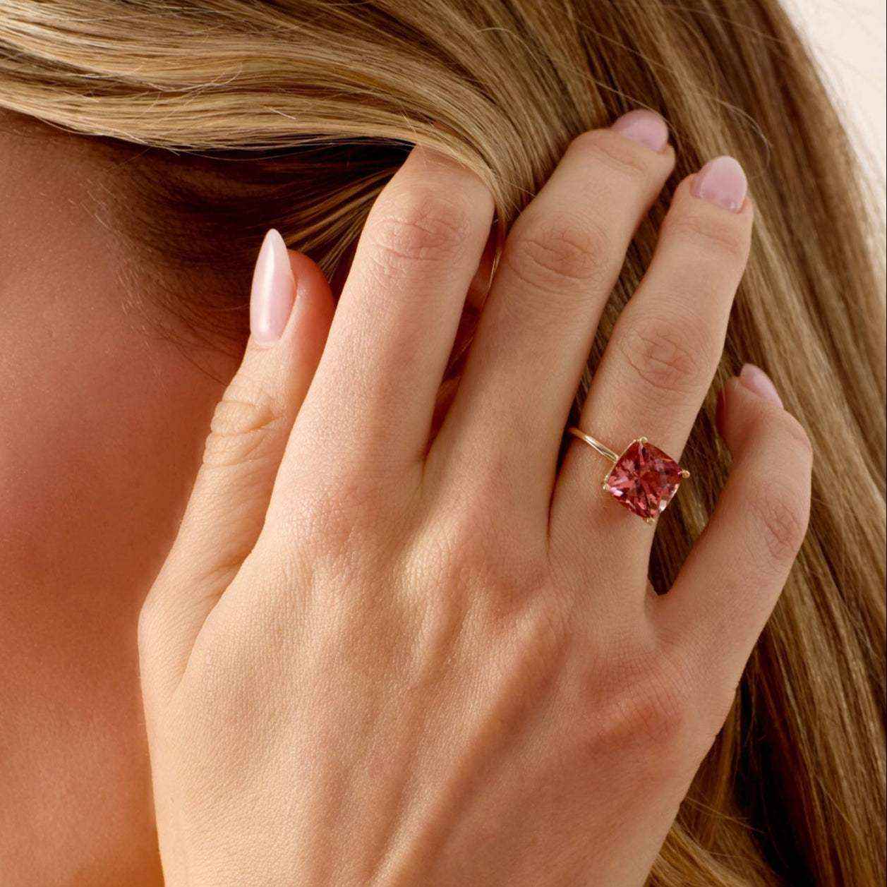 Close-up of a hand wearing a 14k gold Nantucket Red Ring with a cushion-cut pink tourmaline gemstone.