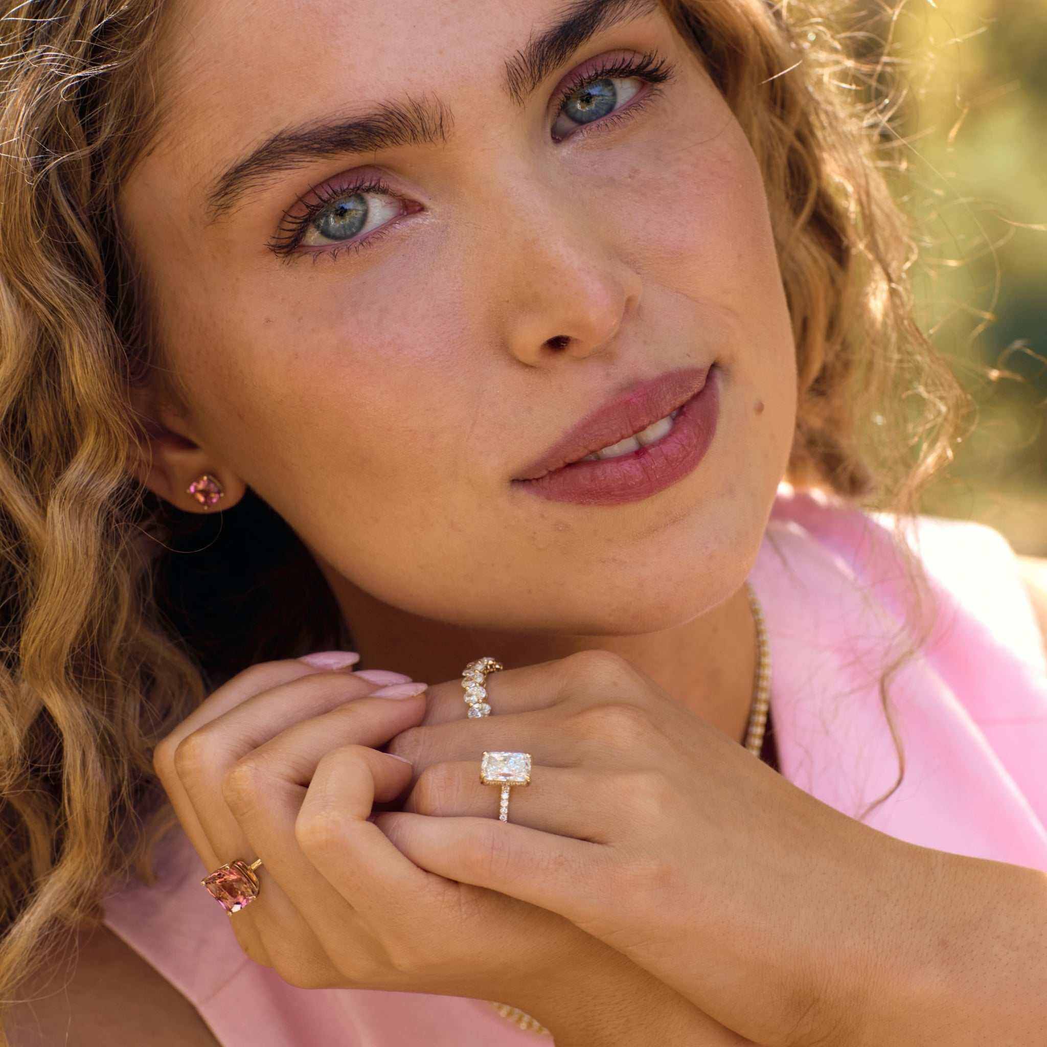 Close-up of woman wearing Nantucket Red Ring with cushion-cut pink tourmaline set in 14k gold, styled with matching pink tourmaline earrings and additional rings.
