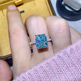 1.8 CTW DEW radiant cut blue green moissanite engagement ring in sterling silver pavé setting on hand
