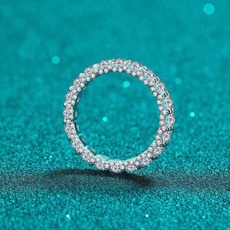 2.1 CTW DEW full round moissanite eternity wedding band in platinum plated sterling silver on sparkling turquoise background