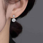 Close-up of ear wearing 1 CTW DEW colorless round cut moissanite halo drop earring in 925 sterling silver with push back stud