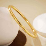 18K yellow gold matte finish round bangle bracelet on beige background