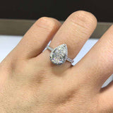 Colorless pear cut moissanite halo engagement ring in sterling silver with pavé accents on finger