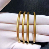 Set of four 18K yellow gold matte finish round bangle bracelets displayed on white gloves.