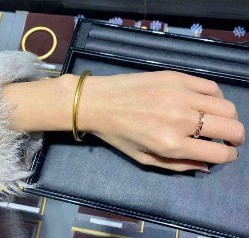 18K yellow gold matte bangle bracelet on wrist with gold ring and black display tray background
