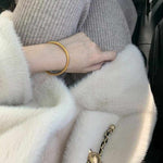 18K yellow gold matte bangle bracelet worn on wrist with grey sweater and white fur coat