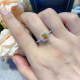 Sterling silver engagement ring with 1 CTW round brilliant yellow moissanite center stone and cushion pavé halo design on finger