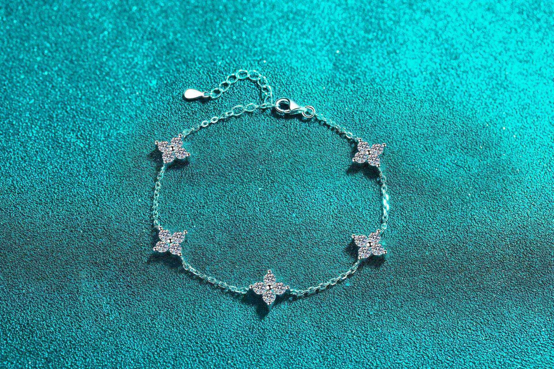 Adjustable sterling silver bracelet with five colorless four-leaf flower moissanite stations on rolo chain
