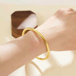 18K yellow gold matte bangle bracelet on wrist with wooden box in background