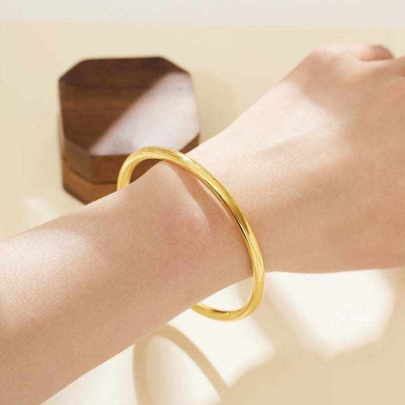 18K yellow gold matte bangle bracelet on wrist with wooden box in background