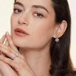 Woman wearing 1 CTW DEW colorless round cut moissanite halo drop earrings in 925 sterling silver with push back studs.