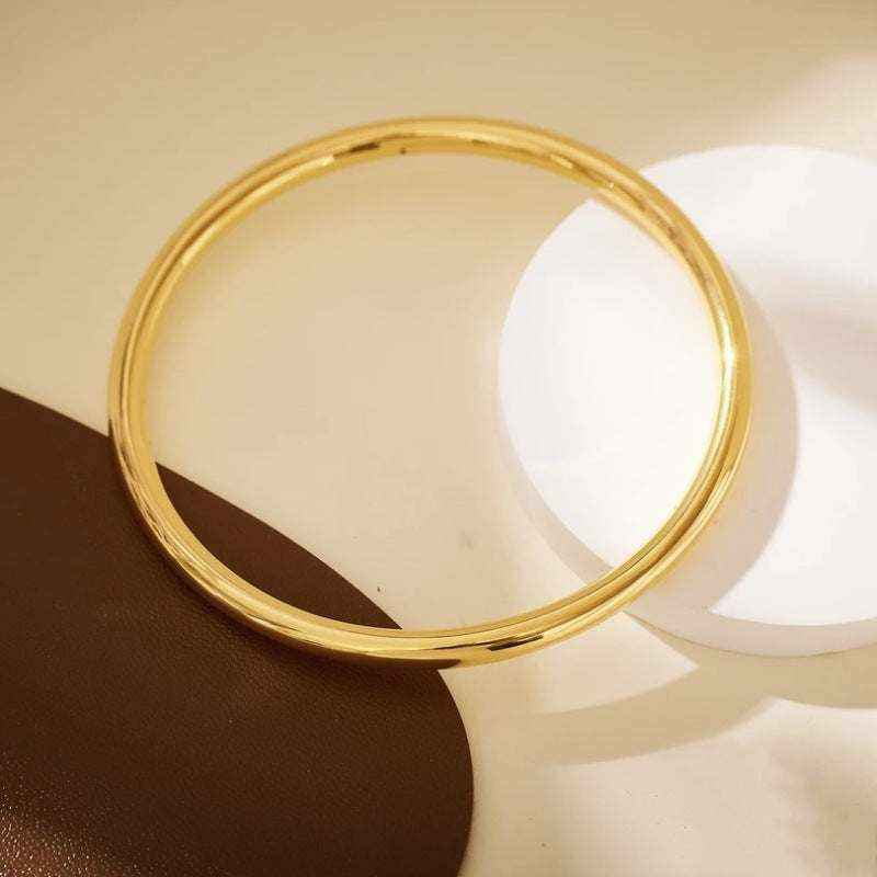 18K yellow gold round matte bangle bracelet with minimalist design on neutral background