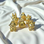 Set of 24K gold Labubu-inspired collectible seated doll pendants with sparkling moissanite accents on white fabric background