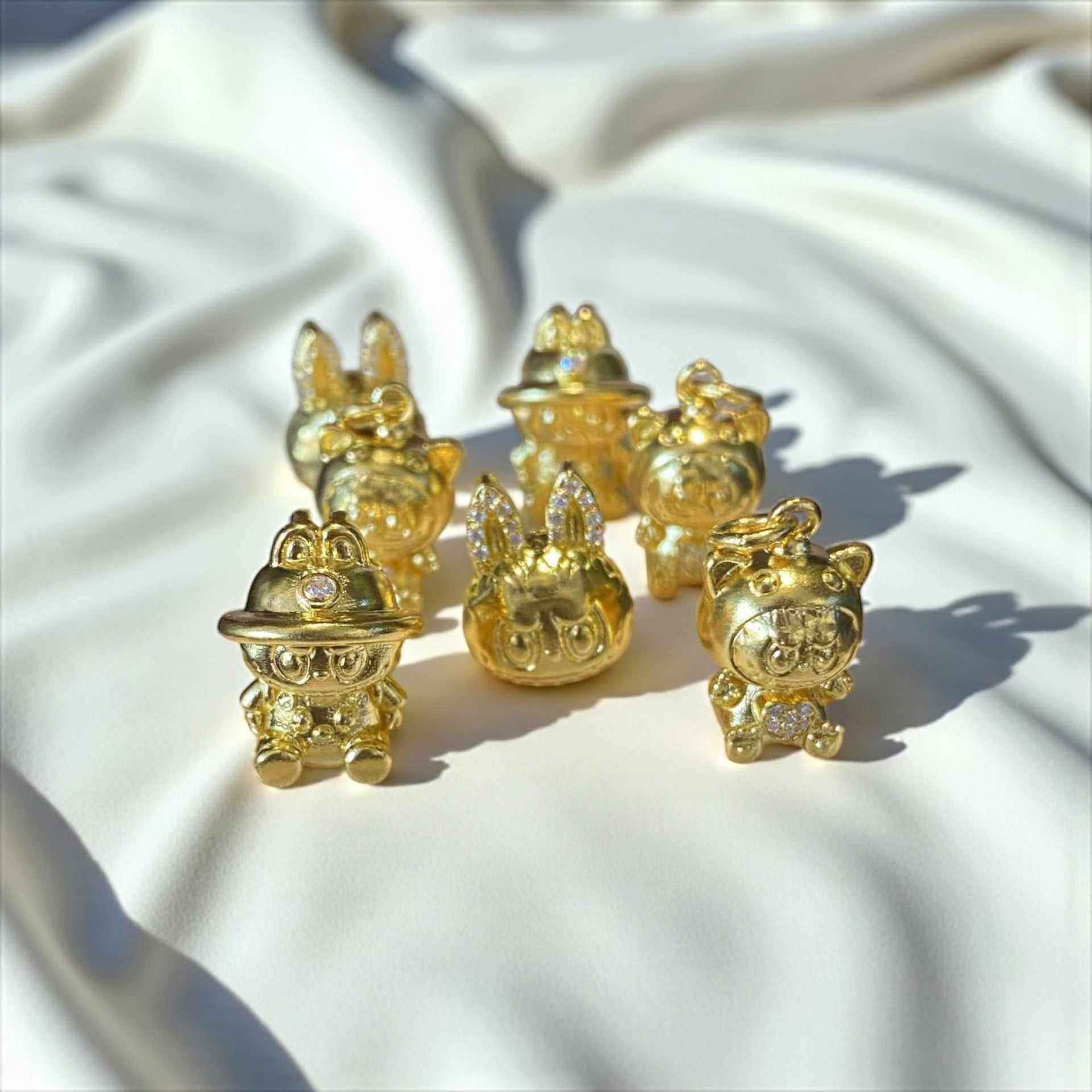 Set of 24K gold Labubu-inspired collectible seated doll pendants with sparkling moissanite accents on white fabric background