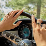 Close-up of hands on steering wheel wearing 14k gold Smokey Quartz rings with cushion-cut stones, showcasing elegant coastal-inspired jewelry design