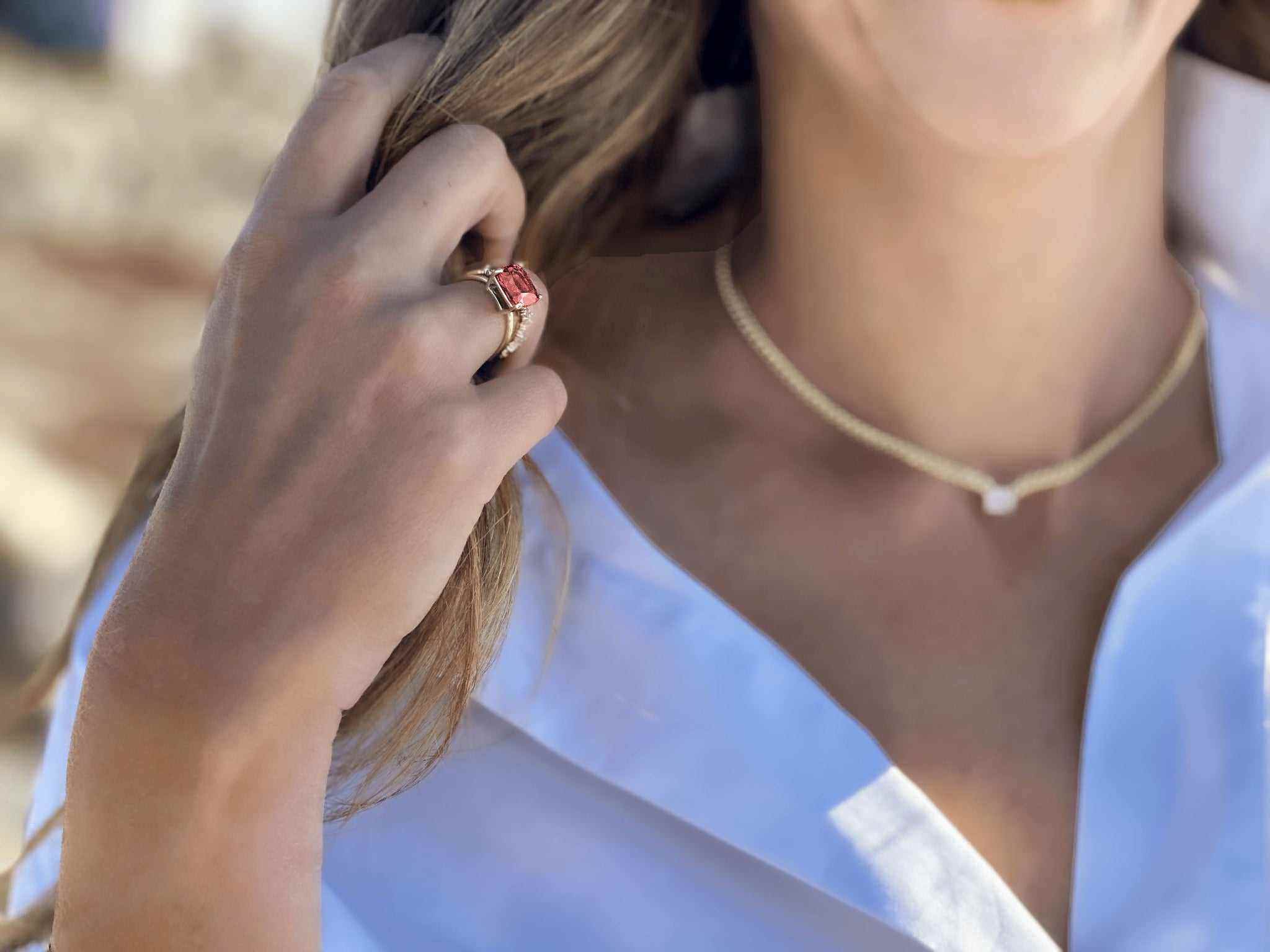 Close-up of a woman wearing the Boston Red Ring with a cushion-cut lab-grown ruby set in 14k gold, styled with a white blouse and gold necklace.