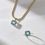 14k gold necklace and ring set with cushion-cut sky blue topaz gemstones on white background