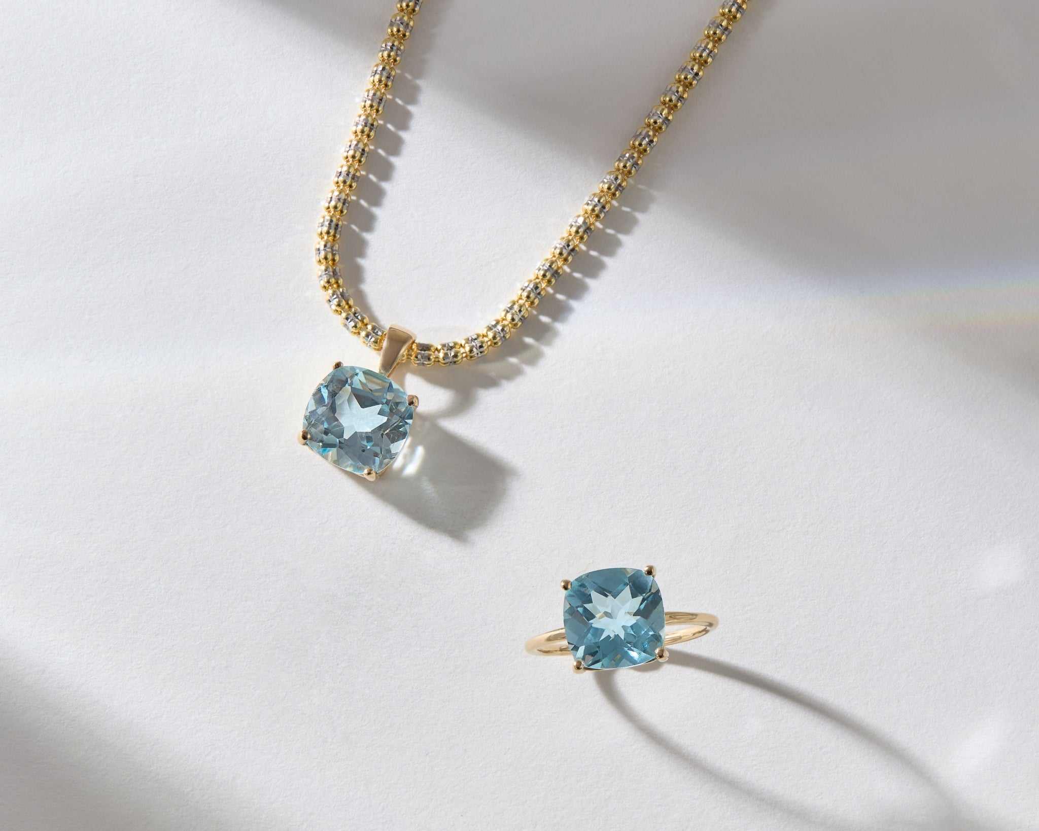 14k gold necklace and ring set with cushion-cut sky blue topaz gemstones on white background