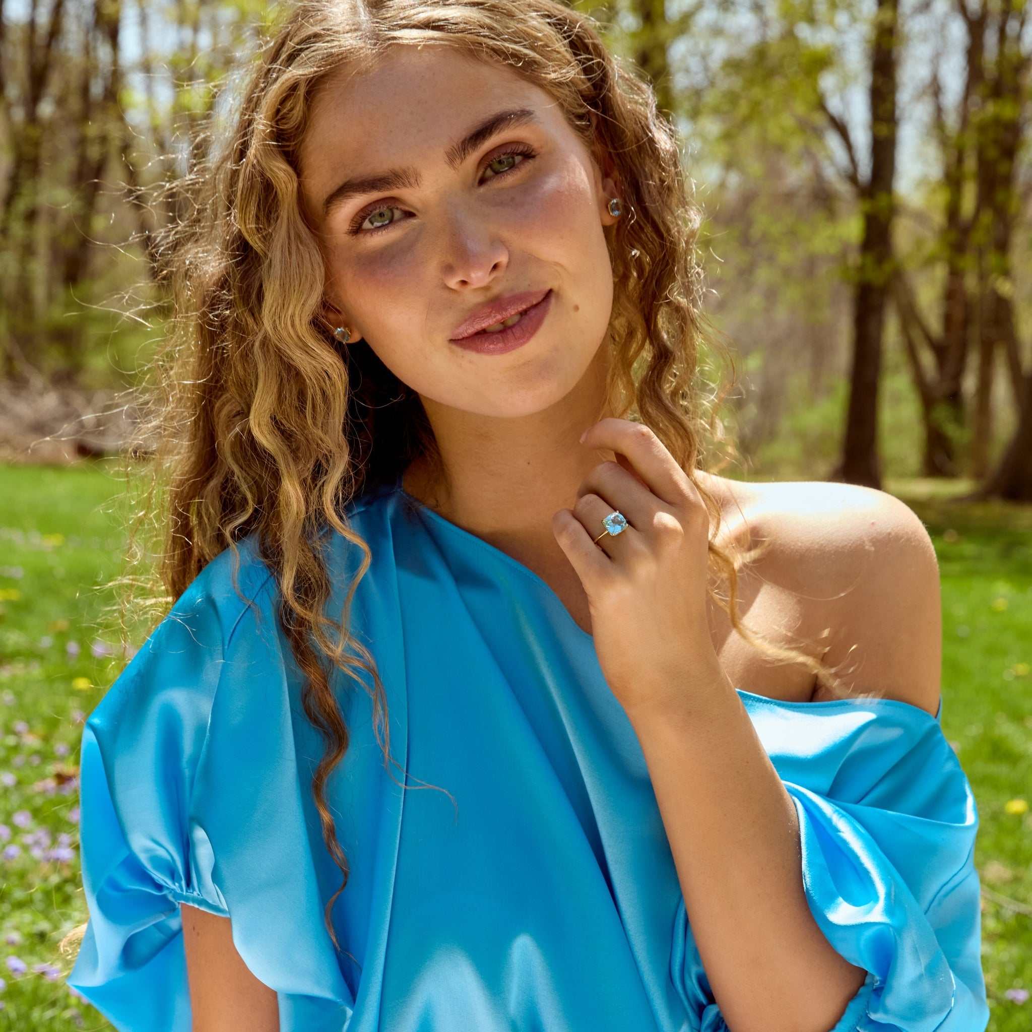 Woman wearing sky light blue topaz ring with 14k gold band and matching blue satin dress outdoors
