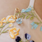 14k gold safety pin pendant with AAA-quality sky blue topaz gemstone on floral embroidered fabric