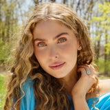 Woman wearing New Hampshire Sky Blue Topaz Tide Earrings and ring with cushion cut blue topaz gemstones in outdoor setting