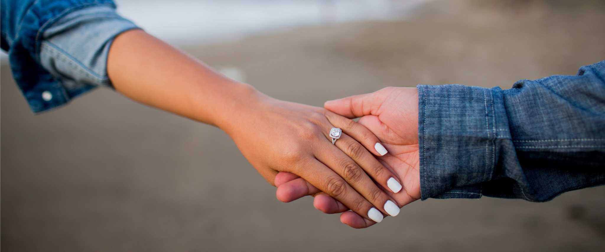 close-up of two hands holding, featuring a diamond engagement ring on one hand symbolizing jewelry protection with Montage Jewelry Care Lifetime Plan