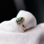 18K yellow gold engagement ring with Australian black opal and halo diamonds showing green, blue, red, and orange colors