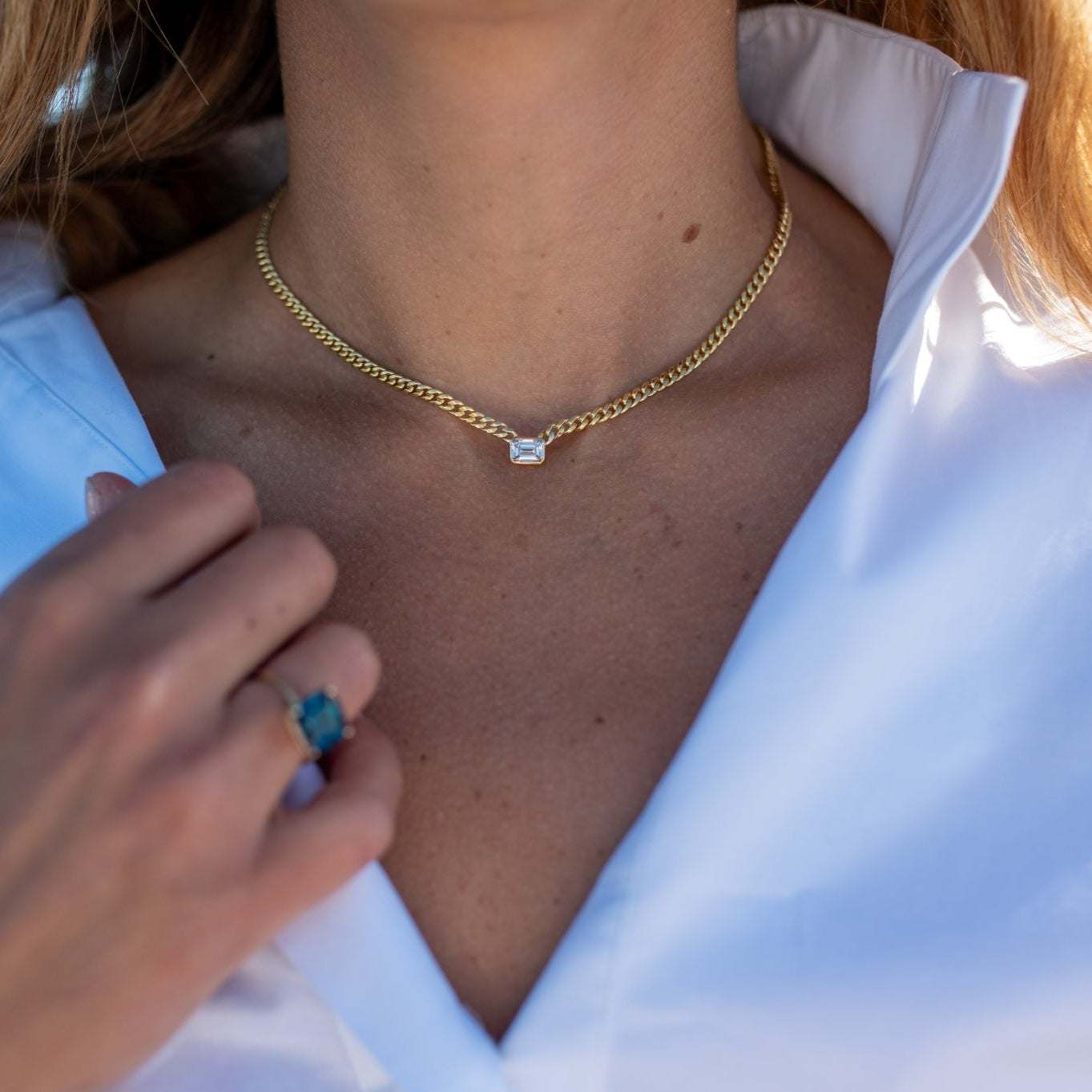 Emerald cut diamond bezel set on a gold Cuban chain necklace worn with white shirt