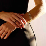 Close-up of a wrist wearing a 5 carat lab grown diamond tennis bracelet in yellow gold with rings, elegant and sparkling jewelry accessory