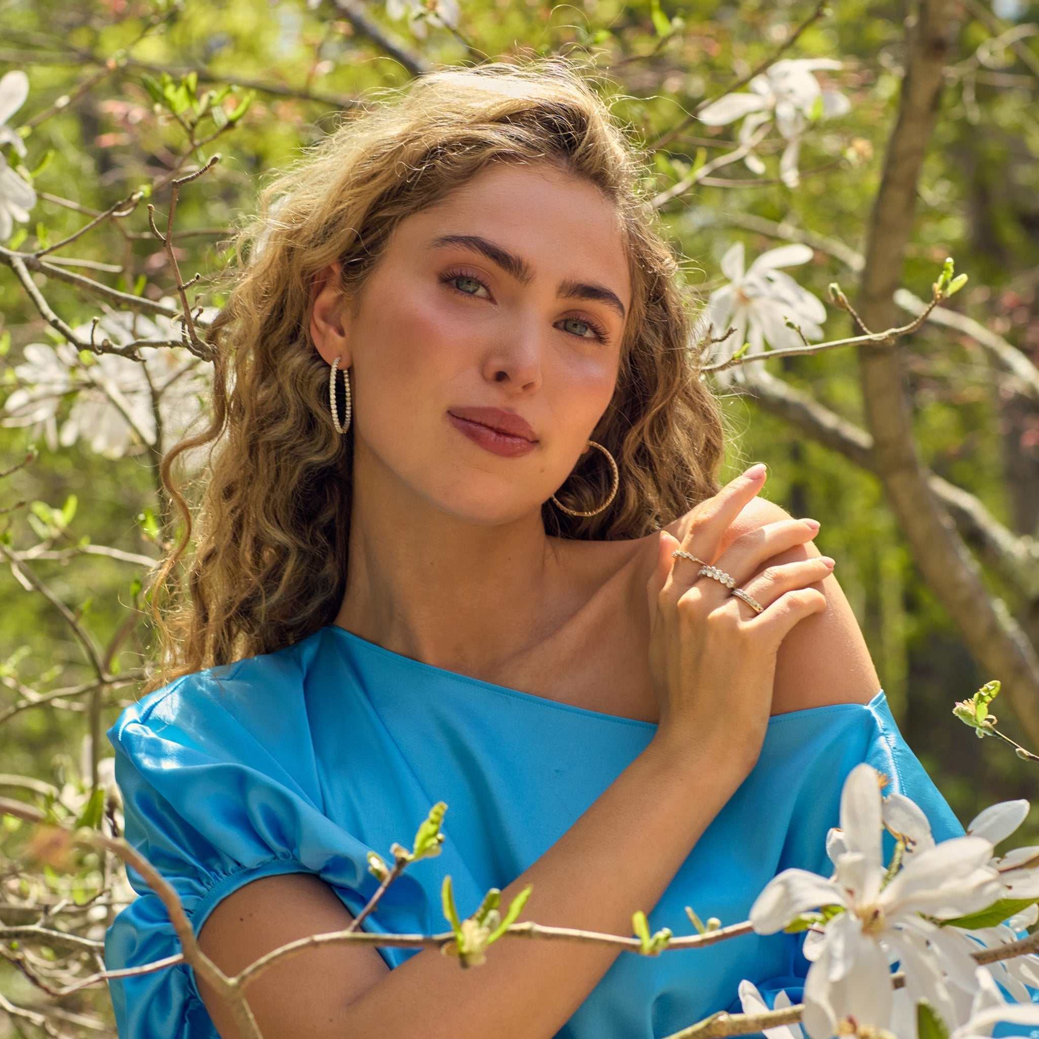 Woman wearing Lighthouse Hoops diamond earrings in front-to-back 14k gold, styled outdoors among blooming branches
