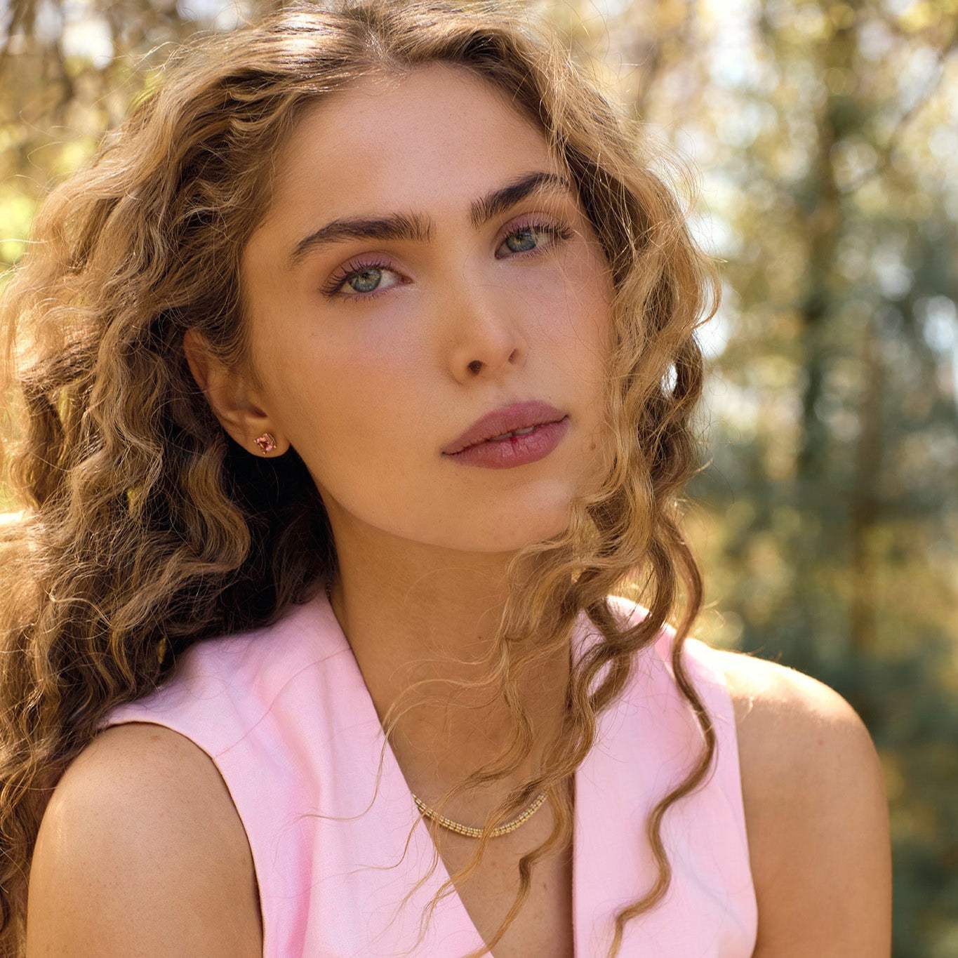 Woman wearing Nantucket Red pink tourmaline cushion cut stud earrings in 14k yellow gold settings outdoors