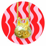 24K gold Labubu-inspired doll-head pendant with sparkling moissanite stones on a gold chain against red and pink wavy background