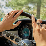 Hands with Nantucket Red Ring featuring cushion-cut pink tourmaline set in 14k gold on a steering wheel.