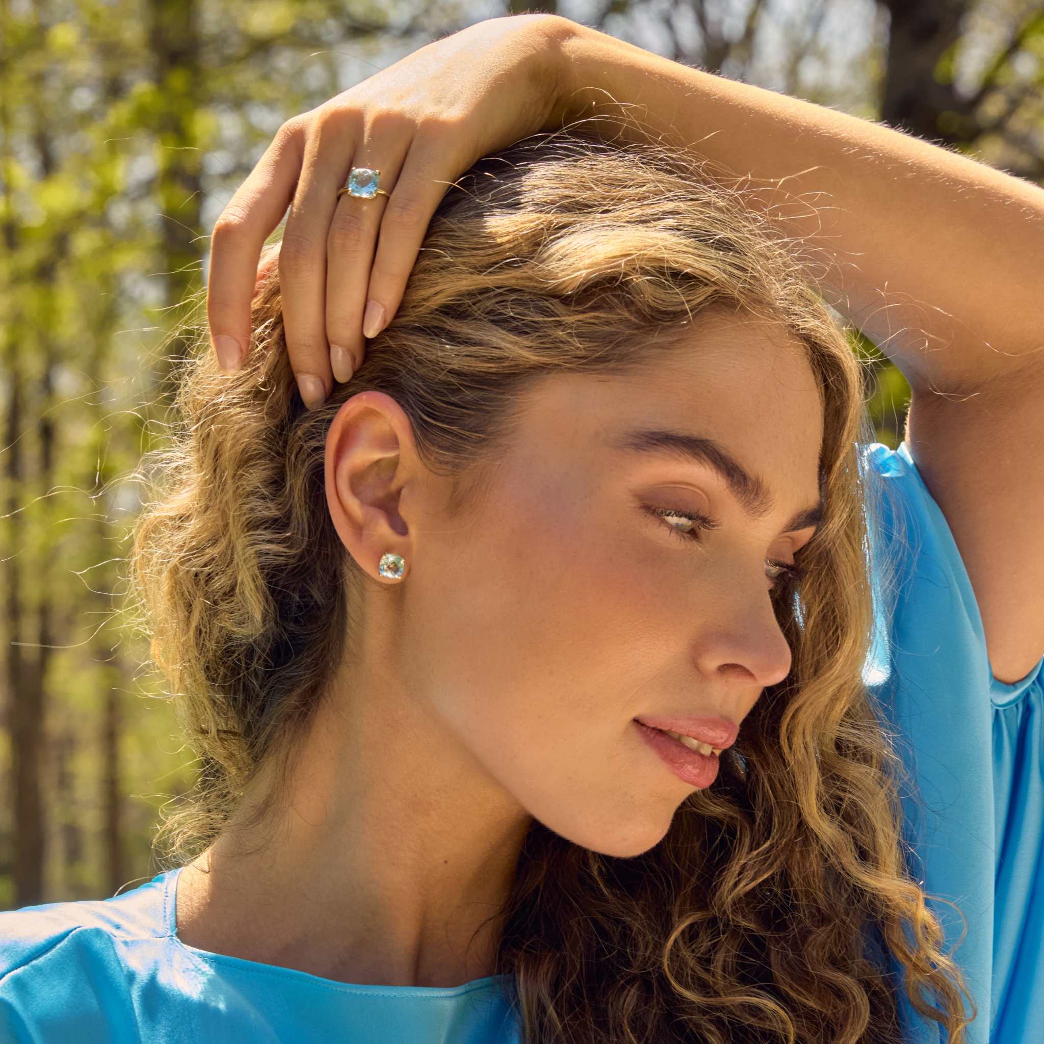 Woman wearing 14k gold cushion cut sky blue topaz stud earrings and matching ring in outdoor setting